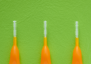 Drei orange Interdentalbürsten mit feiner Borste vor grünem Hintergrund – Hilfsmittel zur Zahnzwischenraumreinigung.